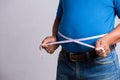 Overweight or fat adult man in very tight jeans with measuring tape on a gray background. Healthcare, medicine concept Royalty Free Stock Photo