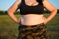 Overweight fat woman in camouflage pants standing outdoors showi
