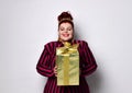 Overweight ginger female in striped dress, crown and earrings. Holding golden gift box, excited, posing isolated on white