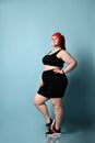 Overweight ginger lady in red headband, black top, shorts, sneakers. Smiling, posing on blue background