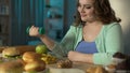 Overweight girl lifting small dumbbell and looking at donut with smirk, diet