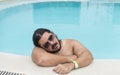 An overweight man dozes off at the side of the swimming pool. Exhausted or bored vacationer