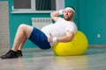 Overweight man is lying on a fitness ball during group fitness classes. Fat man looks satisfied with his result of