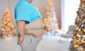 Overweight man measuring his waist in room with Christmas trees after holidays, closeup Royalty Free Stock Photo