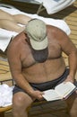 Overweight man reading book while laying in the sun