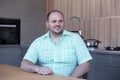 Overweight man sitting at kitchen table and smiles