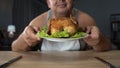 Overweight man smelling greasy grilled chicken with enjoyment, unhealthy food