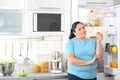 Overweight woman with fresh apple near open refrigerator in kitchen, space for text. Royalty Free Stock Photo