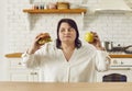 Overweight woman holding apple and burger and choosing between healthy and unhealthy food Royalty Free Stock Photo