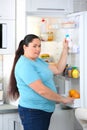 Overweight woman taking yogurt from refrigerator in kitchen Royalty Free Stock Photo