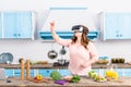 overweight woman in virtual reality headset standing at table with fresh vegetables in kitchen Royalty Free Stock Photo