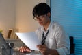 Overwork Concept The office personnel in the loose tie sitting at his desk, reading a paperwork and typing on the notebook Royalty Free Stock Photo