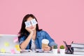 Overworked Asian women. She was sitting at her desk with stickers covering her eyes and using her laptop on a pastel pink Royalty Free Stock Photo