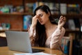 Overworked latin freelancer woman tired after using laptop, working remotely on computer in cafeteria Royalty Free Stock Photo