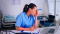 Overworked nurse wrinting on clipboard, working on laptop Royalty Free Stock Photo