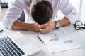 Overworked and tired businessman sitting at workplace with laptop and charts