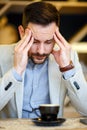 Overworked young businessman having a headache and concentrating while drinking a cup of coffee