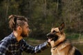 Owner and German Shepherd walk and look at each other devotedly. Young Caucasian hipster with dreadlocks and beard spends time