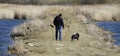 The owner walks his dog near the river.