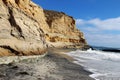 A Pacific coastline with yellow sandstone cliffs and waves rushing the beach