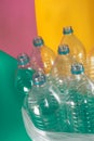 A pack of 7 empty and recyclable plastic water bottles, with no caps, blue seal, in a plastic bag, on a colored pastel