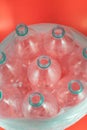 A pack of 8 empty and recyclable plastic water bottles, with no caps, blue seal, inside a plastic bag, on a salmon red