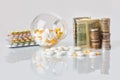 Pack of medicine pills with three packs of coins and glass bottle with dollar cash money