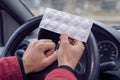 Pack of pills in the hands of the driver on a blurred background of the steering wheel in the car