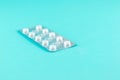 Pack of white pills packed in blister with copy space on turquoise background. Focus on foreground, soft bokeh. Pharmacy drugstore Royalty Free Stock Photo