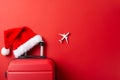 Top-view image of a suitcase, miniature airplane model, and Santa\'s hat on a vibrant red backdrop, offering space