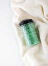 Package of green glitter crystal salt on a bathroom beige towel. Jar of shimmering green sea salt for home spa. Idea of relaxation