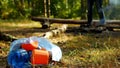 A package with plastic garbage lies on a glade, a fire burns, people walk in the background, camping and nature