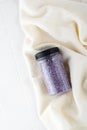 Package of purple shiny crystal salt on a bathroom beige towel. Jar of shimmering purple sea salt for home spa. Idea of relaxation