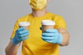 Package to the door. Courier in yellow uniform, protective mask and gloves delivers takeaway coffee.