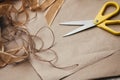 Packaging process. Presents wrapping. Yellow scissors, ribbons, hemp strings and threads, brown craft paper texture background. Royalty Free Stock Photo