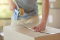 Packed safe and snug. an unidentifiable young man closing a cardboard box with tape at home. Royalty Free Stock Photo