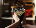 Packet of green coffee is compressed in shape of heart in hands. On the background of coffee accessories. Home roasting