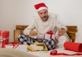 Packing Christmas presents ! young happy and attractive man sitting on bed in Santa Claus hat wrapping and preparing xmas gifts Royalty Free Stock Photo