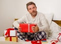 Packing Christmas presents ! young happy and attractive man sitting on bed cozy wrapping and preparing xmas gifts and boxes with Royalty Free Stock Photo