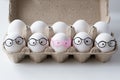 Packing white eggs in a cardboard box. Four eggs in glasses, one egg in rose-colored glasses Royalty Free Stock Photo