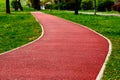 padded red rubber sport and running track floor. soft granular safety flooring. lush green park