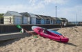 Paddle canoe with oars next to it and beach huts and blue sky as background. Royalty Free Stock Photo