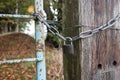 Padlock and chain linking an old metal gate and a wooden pole with barbed wire, blocking the passage to a private area.