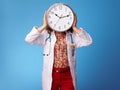 Paediatrist woman holding clock in front of face on blue