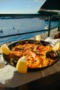 Paella with a huge iron spoon, shrimp and mussels, lemon. On the background of the sea in Spain in summer