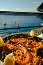 Paella with a huge iron spoon, shrimp and mussels, lemon. On the background of the sea in Spain in summer