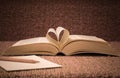 Pages of open book rolled in heart shape on table Royalty Free Stock Photo