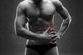 Pain in the left side. Muscular male body. Handsome bodybuilder posing on gray background