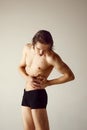 Pains. Young shirtless man standing in underwear, holding hands on belly against grey studio background. Medicine Royalty Free Stock Photo