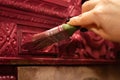 Paint brush in female hand carefully painting amazing wooden ornamented cupboard in red color. Giving new life to old